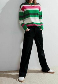 Gebreide trui met horizontale strepen in groen, roze, wit en grijs. Gecombineerd met zwarte rechte broek en witte sneakers.