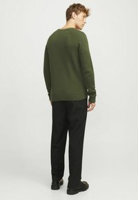 Olijfgroene ribgebreide trui met een ronde hals, gecombineerd met zwarte broek en zwarte schoenen, gezien vanuit de achterkant.