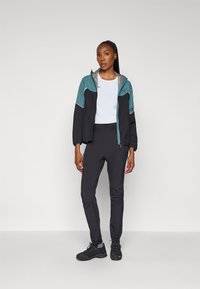Svart og teal glidelåsjakke med satinfinish, sammen med svarte slim-fit bukser og mørke treningssko. Har en hvit T-skjorte med rund hals.