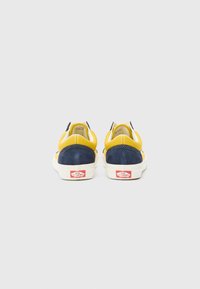 Vans sneakers in yellow and navy blue suede, with a white rubber sole and red logo at the heel. Smooth texture with contrasting panel design.