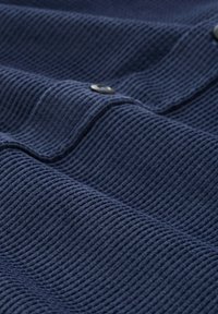 Close-up van marineblauwe corduroy stof met zichtbare ribbels en zwarte knopen langs een naad.