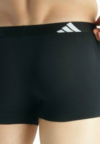 Pantaloni sportivi neri con vita elastica nera, caratterizzati da un design a tre strisce bianche. Tessuto liscio, taglio aderente, senza motivi visibili.