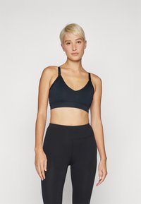 Svart trenings-BH med V-halsdesign og justerbare stropper. Har en glatt tekstur og mykt stoff, kombinert med høy midje svarte leggings.