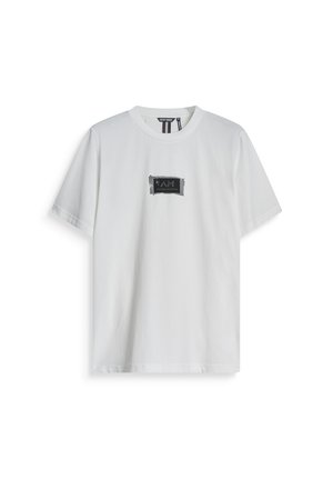 Camiseta de algodón blanca con cuello redondo y mangas cortas, con un parche de logo rectangular negro que dice "I AM".