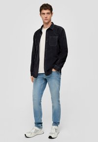 Czarna koszula ze sztruksu z kieszenią na piersi, zestawiona z jasnoniebieskimi dżinsami i białymi trampkami z szarymi akcentami. Casualowy krój i wzór.