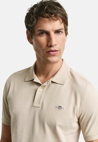 Polo shirt beige in cotone con finitura texture. Presenta un colletto con bottoni e un piccolo logo ricamato sul petto.