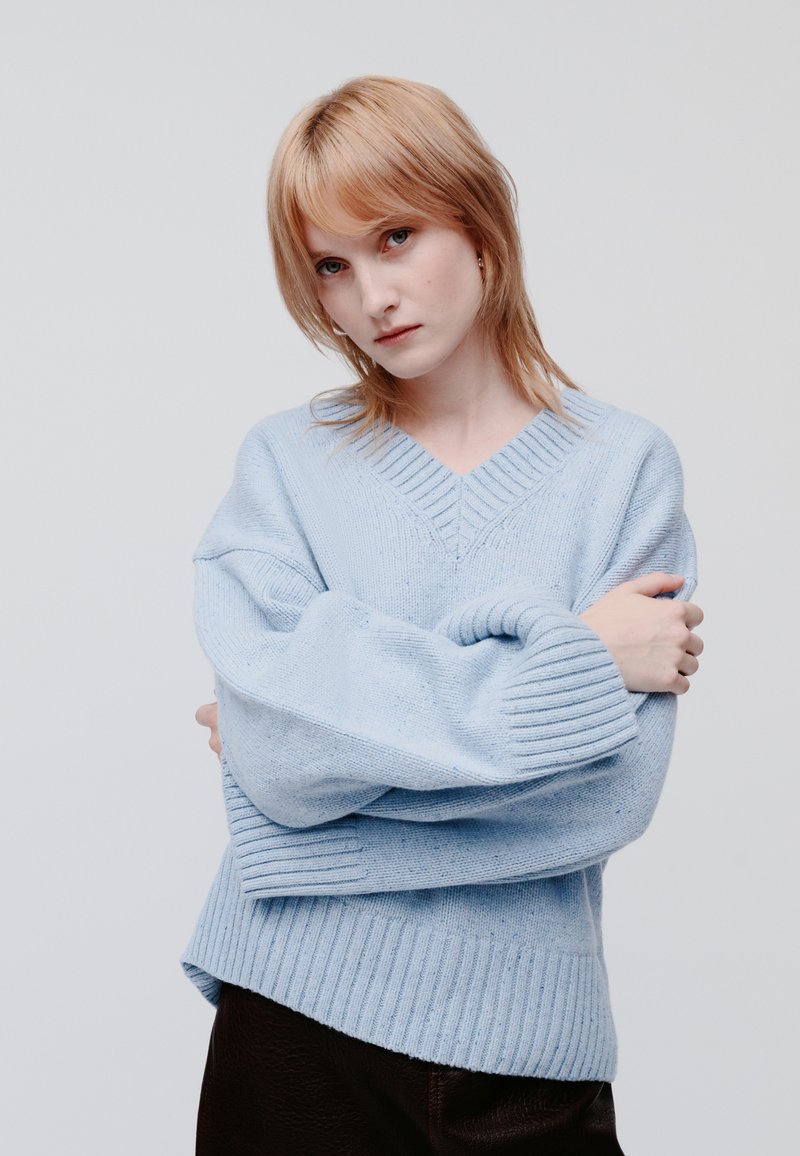 Light blue knitted sweater featuring a V-neck, ribbed cuffs, and a textured finish, paired with dark brown leather pants.
