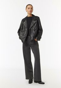 Schwarze Leder-Doppeltknopfjacke mit breiten Revers, kombiniert mit eng anliegenden dunkelblauen Jeans und knöchelhohen schwarzen Stiefeln.