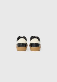 Black leather sneakers with white accents, rounded backs, and rubber soles. Smooth texture with subtle stitching details. Casual design.