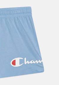 Shorts bleu clair en tissu doux, avec une taille élastique et un grand logo "Champion" blanc avec un accent rouge.