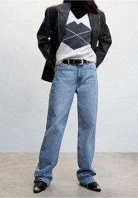 Jeans de pierna recta azul claro, combinados con un blazer negro y un suéter de patrón que presenta formas de diamante en gris y crema. Botas negras de punta.