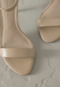 Sandales beiges à lanières avec un semelle texturée et un bout lisse et arrondi. Design minimaliste avec une large lanière sur le devant du pied.