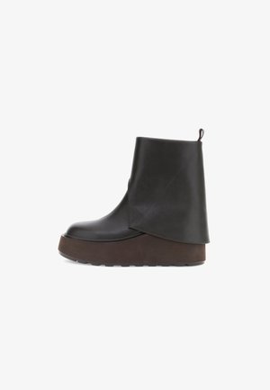 Bottine en cuir noir avec un design empilé unique, présentant une épaisse semelle plateforme marron et une languette à l'arrière.