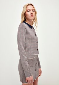 Kortärmad cropped jacka och matchande kjol i vävt tyg med ett rutmönster i röd, blå och vit med marinblå detaljer och knappar.