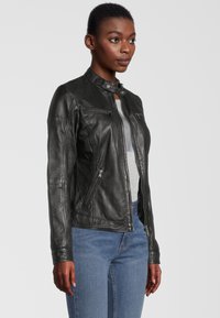 Schwarze Lederjacke mit Stehkragen, frontale Reißverschlussöffnung und zwei Reißverschlusstaschen. Glatte Textur und taillierte Passform mit Nähdetails.