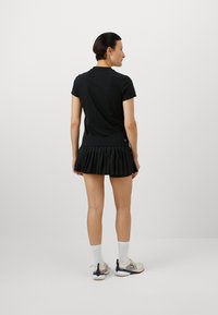 Maglietta nera a maniche corte con una gonna plissè nera. L'outfit presenta una vestibilità comoda e una gonna tessurizzata, abbinata a sneaker leggere.
