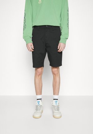Black knee-length shorts with a relaxed fit, made from cotton blend fabric. Paired with a long-sleeve green jersey and white high-top sneakers.