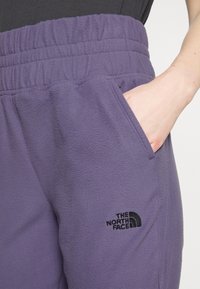 Lila Fleece-Trainingshosen mit elastischem Bund. Mit seitlichen Taschen und einem schwarzen gestickten Logo auf dem Oberschenkel. Weiche Textur.