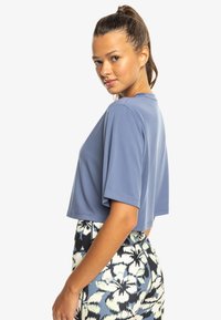 Light blue cropped t-shirt with short sleeves, round neckline, and smooth texture, paired with patterned high-waisted pants in blue and white.