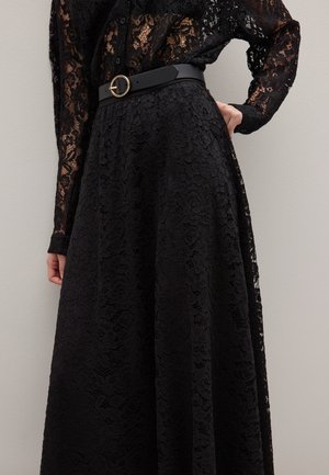 Schwarzes Spitzenkleid mit langen Ärmeln, Blumenmuster und vollem Rock, kombiniert mit einem schwarzen Gürtel mit einer goldenen, runden Schnalle.