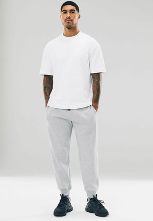 Witte katoenen t-shirt met korte mouwen, gecombineerd met lichtgrijze joggers met zakken en geribbelde manchetten, gedragen met zwarte sneakers.