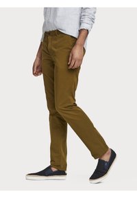 Pantalons kaki en coton, avec une coupe ajustée et un devant plat, associés à des chaussures sans lacets bleu marine avec une texture tissée et des semelles blanches.