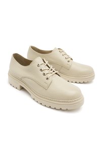Beżowe skórzane buty na sznurówki o teksturowanej powierzchni, zaokrąglonym nosku i grubej gumowej podeszwie z mocnymi detalami i kontrastowym przeszyciem.