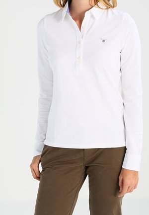 Weißes langärmliges Poloshirt mit Knopfleiste und kleinem Logo auf der Brust. Weicher Baumwollstoff, klassischer Kragen und taillierte Passform.