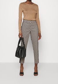 Maglia marrone a maniche lunghe abbinata a pantaloni neri e crema a fantasia. Gli accessori includono una borsa nera arricciata e tacchi aperti neri.