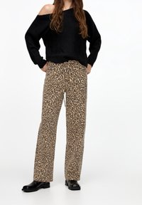 Pull noir en maille à épaules dénudées, associé à un pantalon beige imprimé léopard à jambes larges et des bottines en cuir noir.