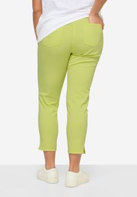 Grüne Cropped-Jeans mit glatter Textur, zwei Gesäßtaschen und seitlichen Schlitzen am Saum, kombiniert mit weißen Sneakers.