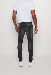 Černé džíny slim fit s vybledlým efektem, dvěma zadními kapsami a mírným ošoupáním, doplněné světle šedým tričkem a bílými teniskami.