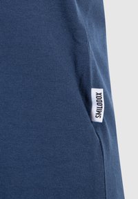 T-shirt blu navy realizzato in morbido cotone con superficie testurizzata, caratterizzato da un'etichetta bianca sul lato con la scritta "SMILOOX".