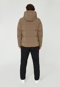 Brun puffjacka med huva, med en quiltad design. Bärs med svarta byxor och vita sneakers, vilket ger en avslappnad, lager-på-lager look.