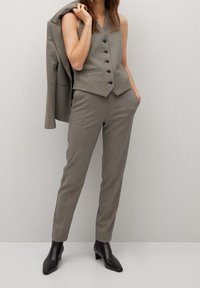 Chaleco gris a medida con cinco botones y dos bolsillos, combinado con pantalones ajustados a juego y botas negras hasta el tobillo. Textura de tela suave.