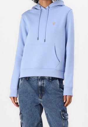 Osoba ubrana w jasnoniebieską bluzę z kapturem z kieszenią z przodu i sznurkami, w połączeniu z luźnymi niebieskimi dżinsowymi spodniami typu cargo.
