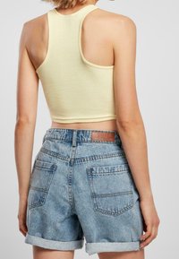 Top corto a righe giallo abbinato a pantaloni denim chiari, con orli arrotolati e due tasche posteriori con etichetta marrone.