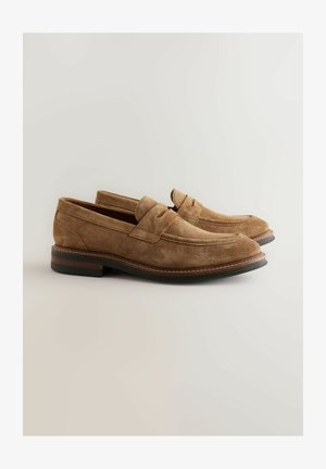 Ein Paar hellbraune Wildleder-Pennyloafer mit gesteppten Details und niedrigen, gestapelten Holzabsätzen auf einem schlichten, hellen Hintergrund.