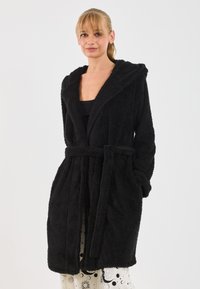 Rochie de baie neagră, pufoasă, cu glugă, talie închisă cu un cordon și două buzunare frontale. Textură moale și design de lungime medie.