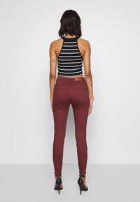 Top de halter a rayas en blanco y negro, pantalones burdeos ajustados, tiras de tobillo, bolsillos traseros, parche de cuero en la cintura, textura de tela suave.