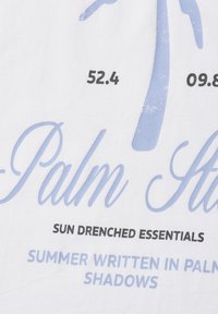 Texte sur tissu blanc comprenant les chiffres "52.4" et "09.8", un palmier bleu stylisé et les phrases "Sun Drenched Essentials" et "Summer written in palm shadows."