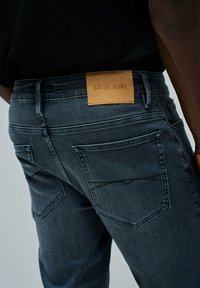 Jeans de mezclilla oscura con una textura distintiva, que cuentan con una etiqueta de cuero marrón claro marcada "SALSA JEANS" y dos bolsillos traseros.