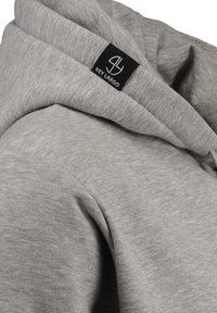 Felpa grigia con una texture morbida, dotata di cappuccio e di un'etichetta nera con logo bianco. Il design enfatizza la semplicità e il comfort.