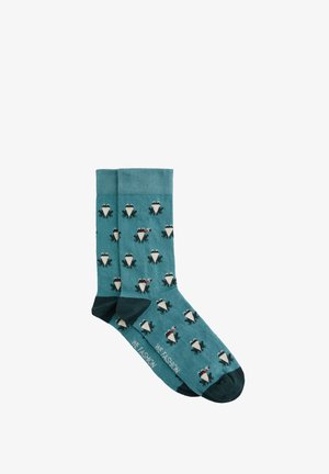 Türkise Socken mit einem sich wiederholenden Muster von Pinguinen mit roten Akzenten, aus einem weichen Strickmaterial gefertigt, mit kontrastierenden dunklen Zehen und Fersen.