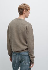 Bruine gebreide trui met een ronde hals, ribgebreide boorden en zoom. Draagt bij lichte blauwe denim jeans, met achterzakken. Schoon, minimalistisch ontwerp.