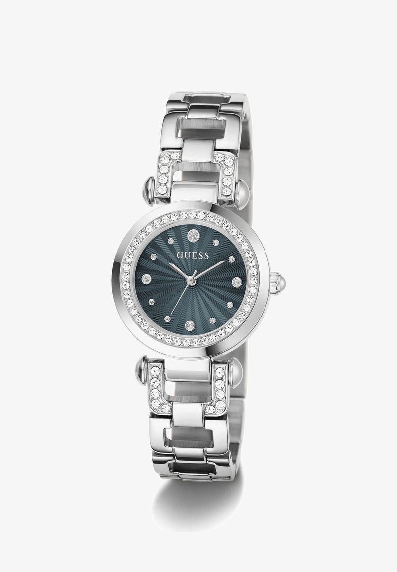 Ασημένιο ρολόι χειρός Guess με σκούρο υφασμάτινο καντράν, ενδείξεις ώρας από κρύσταλλα και στεφάνη και κρίκους μπρασελέ στολισμένους με κρύσταλλα.