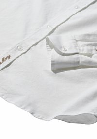 Camisa de algodón blanca de manga larga con una textura suave, que cuenta con cierres de botones, puños doblados y un sutil detalle bordado.