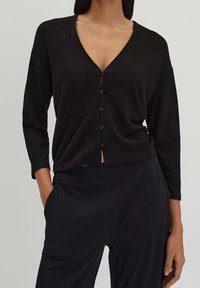 Černý žebrovaný kardigan s hlubokým výstřihem do V, dlouhými rukávy a zapínáním na pět knoflíků, vyrobený z měkkého materiálu a zkrácený do délky pasu.