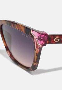 Lunettes de soleil en écaille de tortue avec des verres dégradés violets, finition brillante et branches accentuées de rose avec un détail de marque couleur or.
