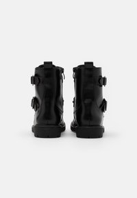Bottines en cuir noir avec une finition lisse, dotées de deux sangles latérales, d'une fermeture éclair et d'une semelle en caoutchouc robuste. Vue arrière montrée.